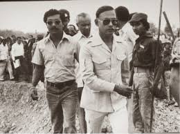 Ziaur Rahman in a light safari suit and sunglasses visiting a rural or construction site with officials and onlookers.